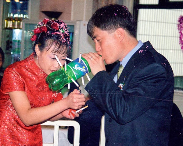 A film photograph of a Chinese bride lighting a series of cigarettes in a Sprite softdrink bottle, held by a man in a suit.